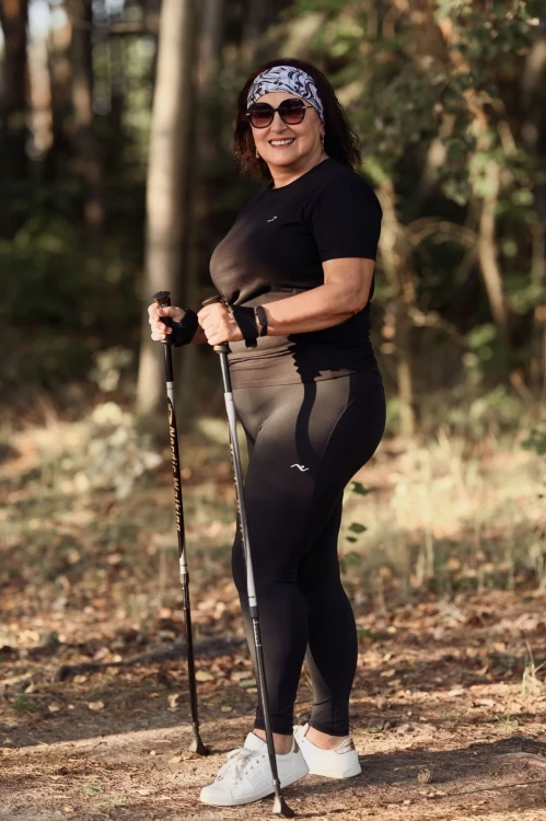 Seniorka w legginsach ActiveGlow spaceruje z kijami, ujęcie podczas aktywności na świeżym powietrzu