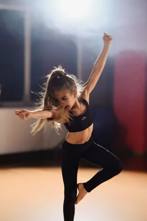 Modelka w dynamicznej tanecznej pozie, czarne legginsy dziewczęce ActiveGlow z przeszyciami