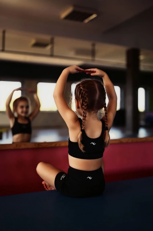 Mała modelka siedzi przed lustrem do tańca w czarnych szortach dziewczęcych ActivGlow