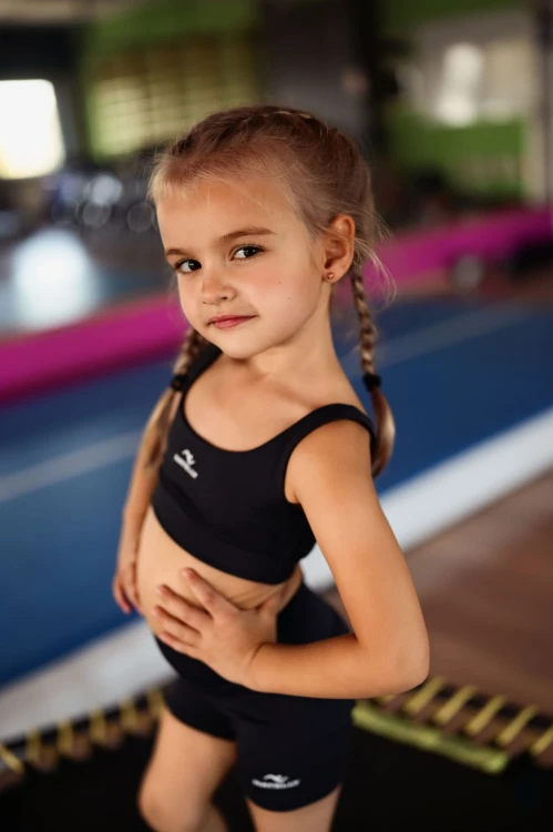 Mała modelka w topie dziecięcym Natelly pozuje na sali gimnastycznej