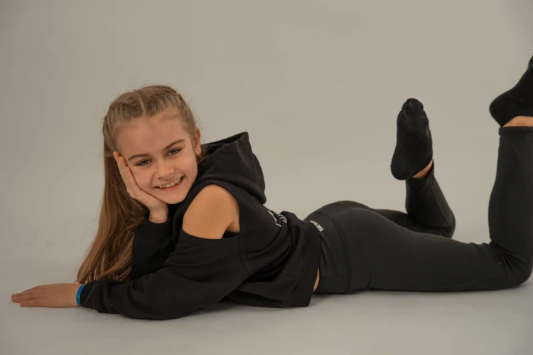 Bluza dziewczęca FLOW z odkrytymi ramionami czarna - modelka leży na brzuchu