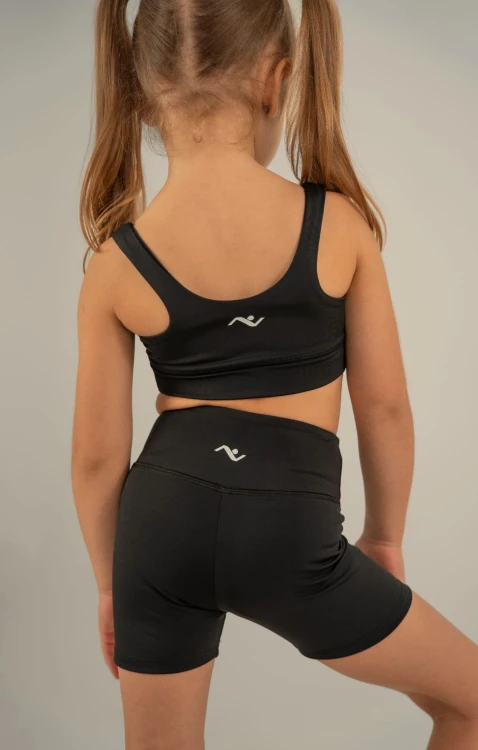 Mała modelka tyłem w czarnych krótkich getrach dziewczęcych