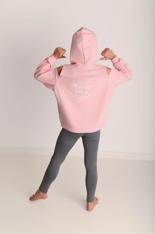 Bluza dla dziewczynki z odkrytymi ramionami pudrowy róż - modelka stoi tyłem w kapturze
